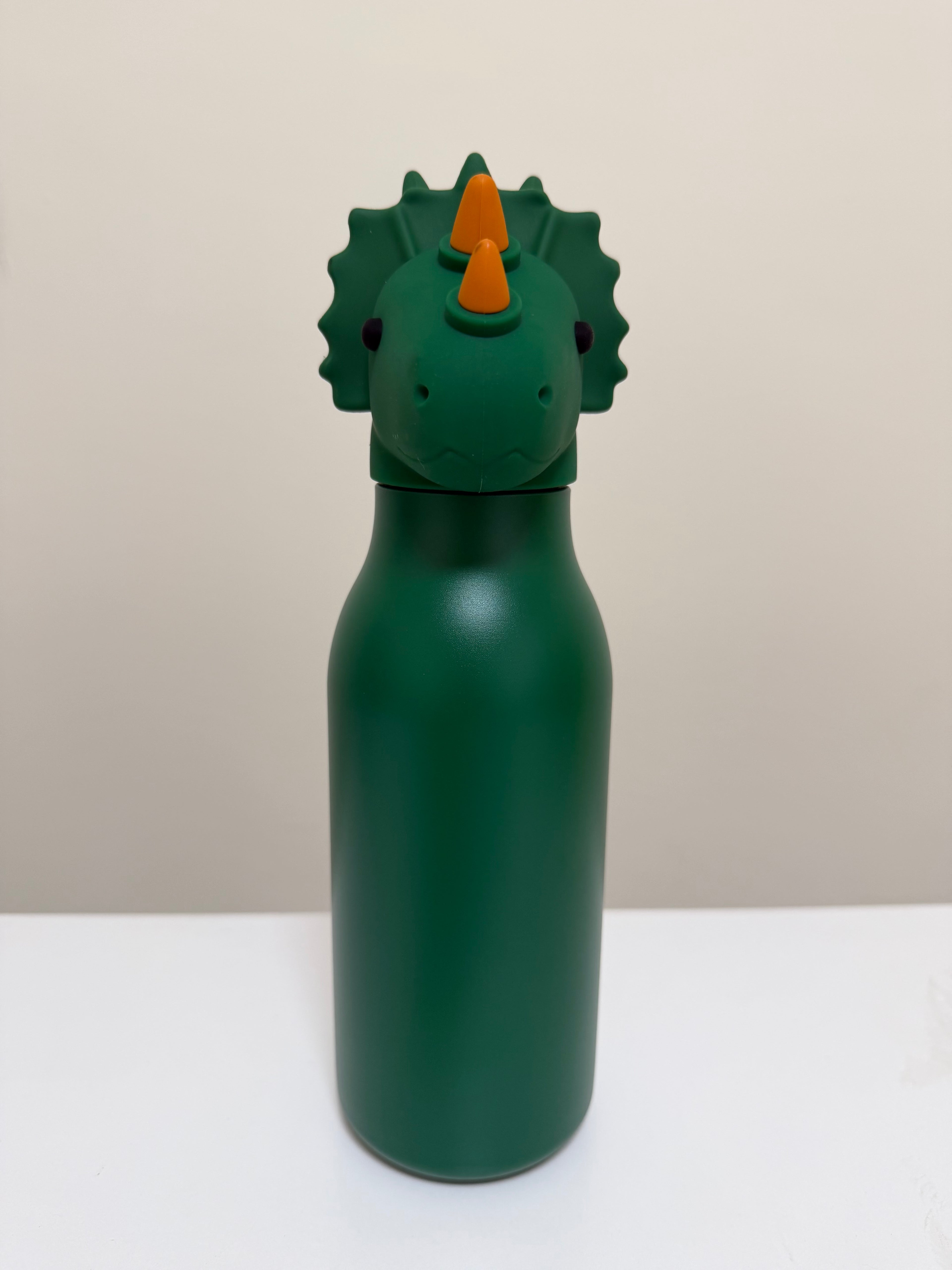 A dark green bottle with a dinosaur head lid featuring a green frill, a dark green face, and orange horns, set against a neutral beige and white background.