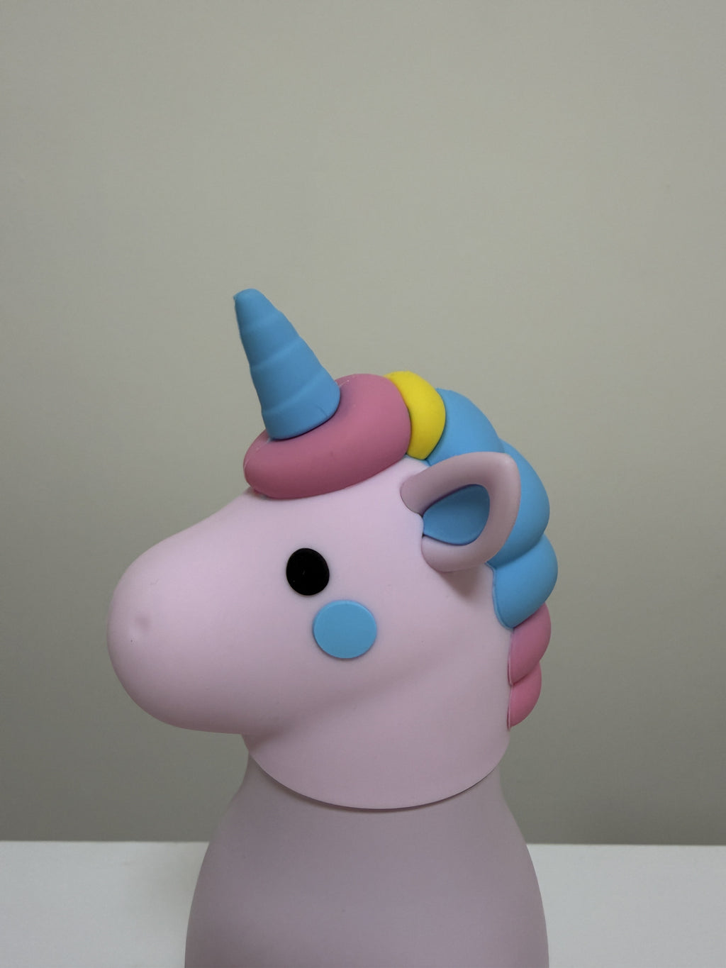 A pastel unicorn head wall-mounted holder or decor piece in pink, blue, purple, yellow, and pink, shown against a plain beige wall.