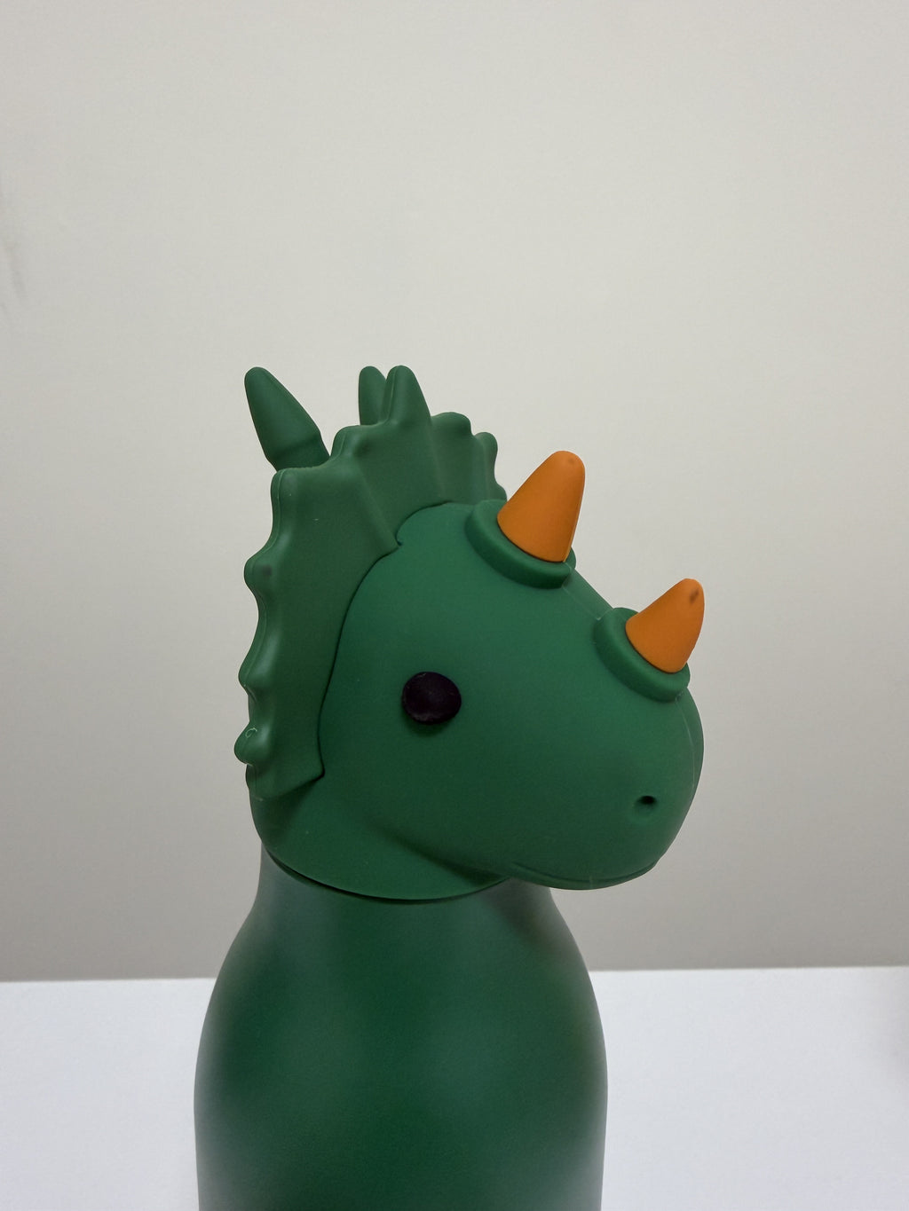 A green dinosaur toy with orange horns and a small black eye, shown in profile against a plain light gray background.