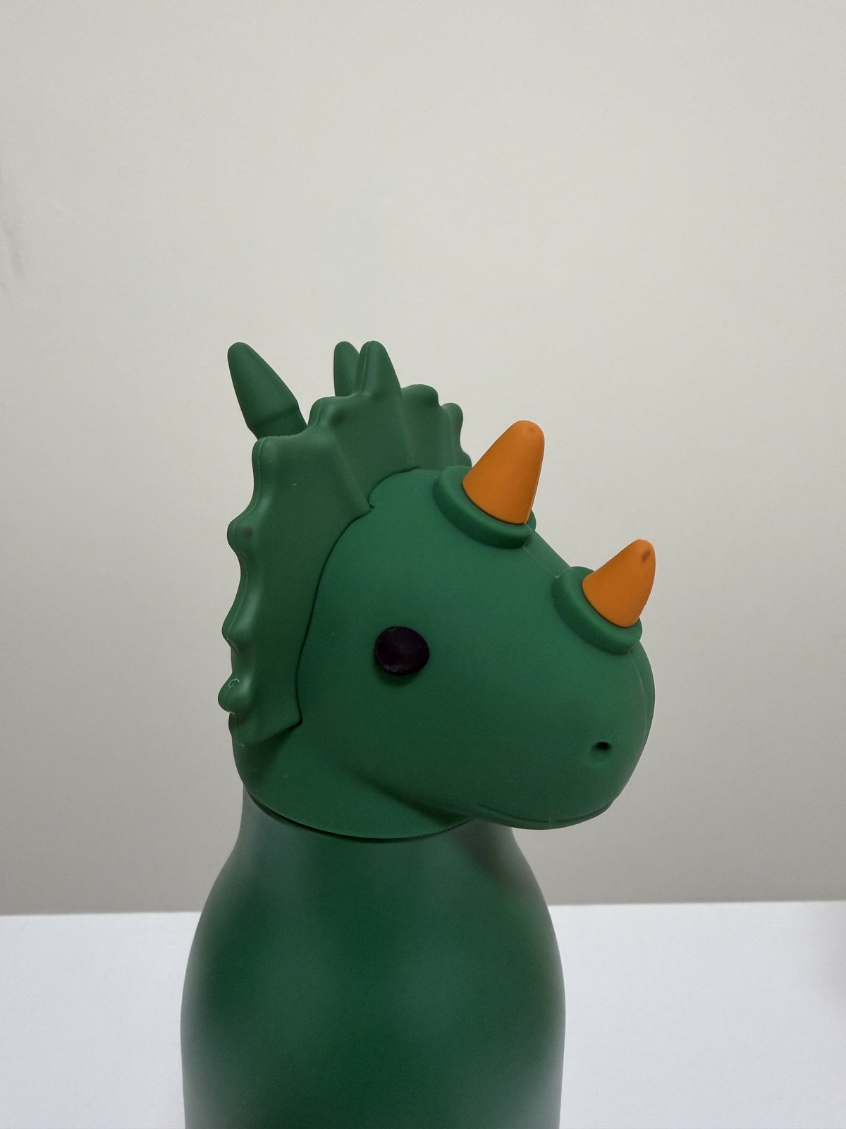 A green dinosaur toy with orange horns and a small black eye, shown in profile against a plain light gray background.